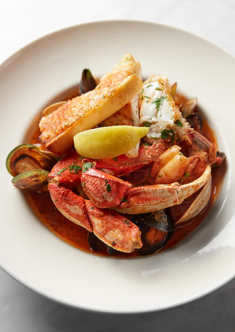Bowl of cioppino with crab claws, mussels, clams, shrimp, and garlic bread