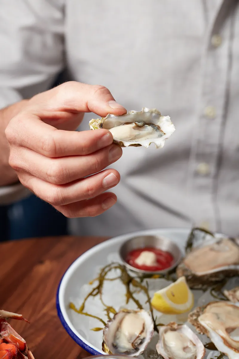 Hand holding a freshly shucked oyster over a plate of oysters on ice